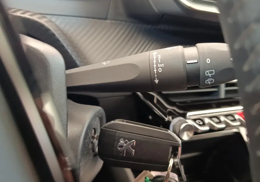 Gros plan intérieur sur la clé insérée dans le contacteur d'une Peugeot 208, avec commandes de phares et tableau de bord en arrière-plan.