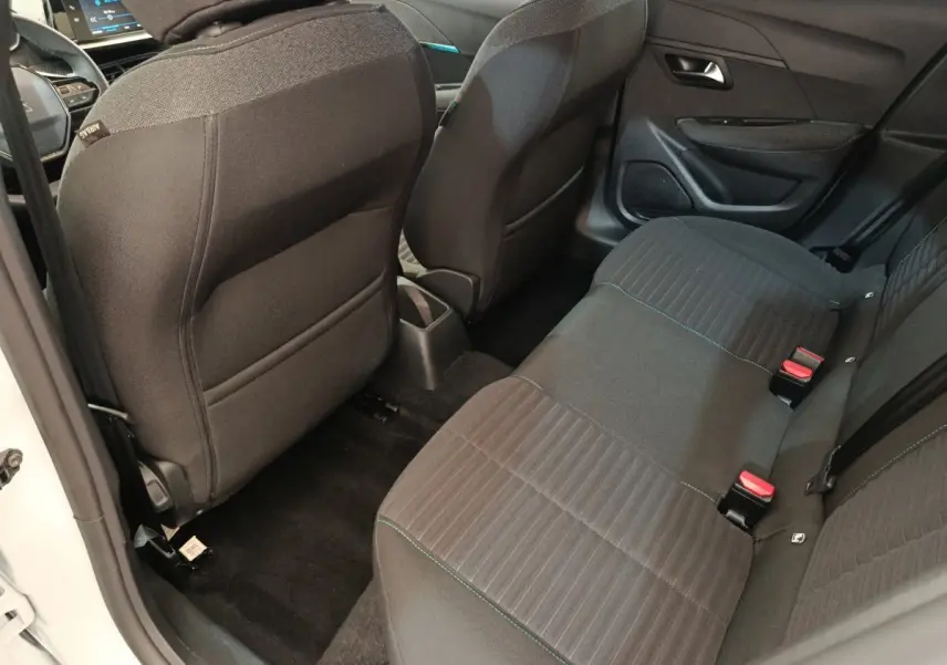 Vue intérieure arrière côté gauche de la Peugeot 208 2023 avec sièges tissu noir et ceintures rouges visibles.