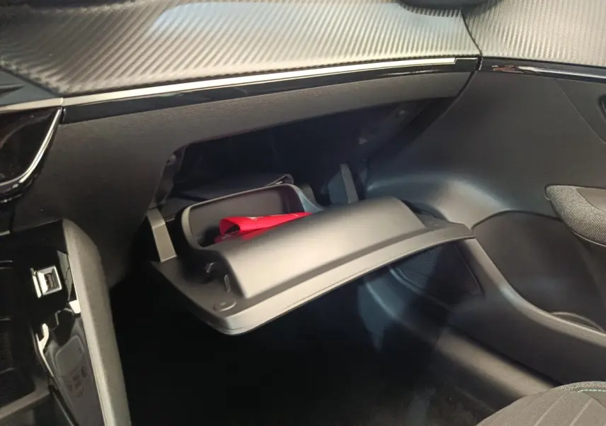 Intérieur de la Peugeot 208 PureTech 75 S&S Style 2023, vue sur la boîte à gants ouverte côté passager avec un objet rouge à l'intérieur.