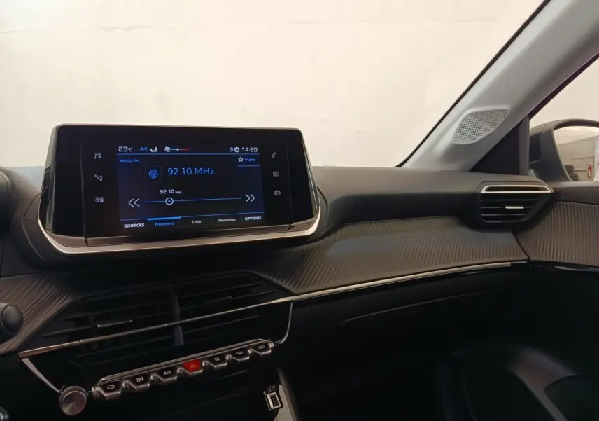 Vue intérieure côté passager du tableau de bord noir de la Peugeot 208 2023 avec écran tactile central allumé.