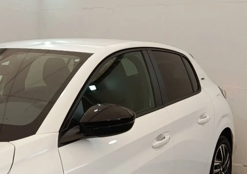 Vue de côté gauche rapprochée d’une Peugeot 208 blanche avec rétroviseur noir brillant et vitres teintées.