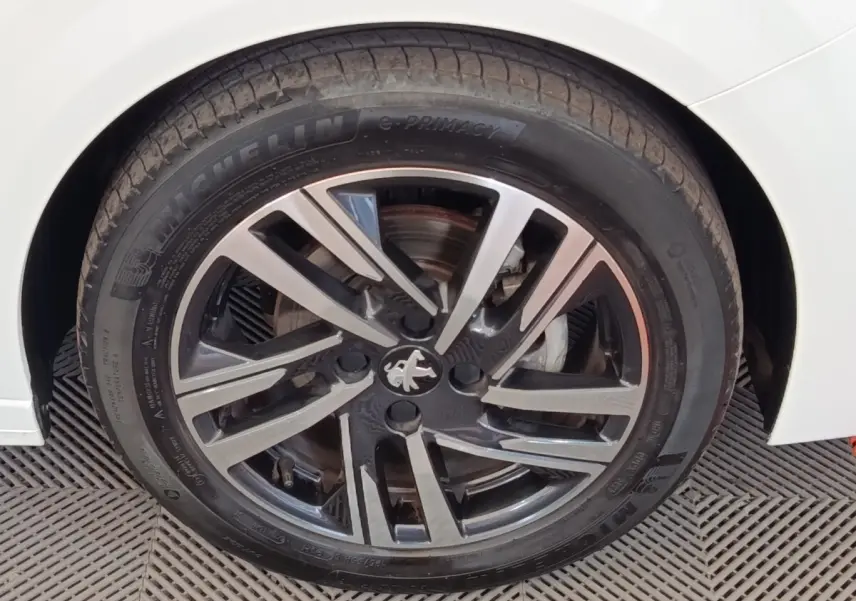 Gros plan sur la roue avant droite d'une Peugeot 208 blanche avec jante alliage noire et argentée au design moderne.