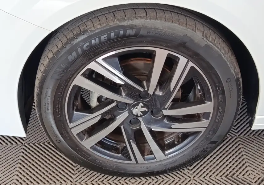 Gros plan sur la roue avant droite d’une Peugeot 208 blanche avec jante alliage noire et argentée au design moderne.