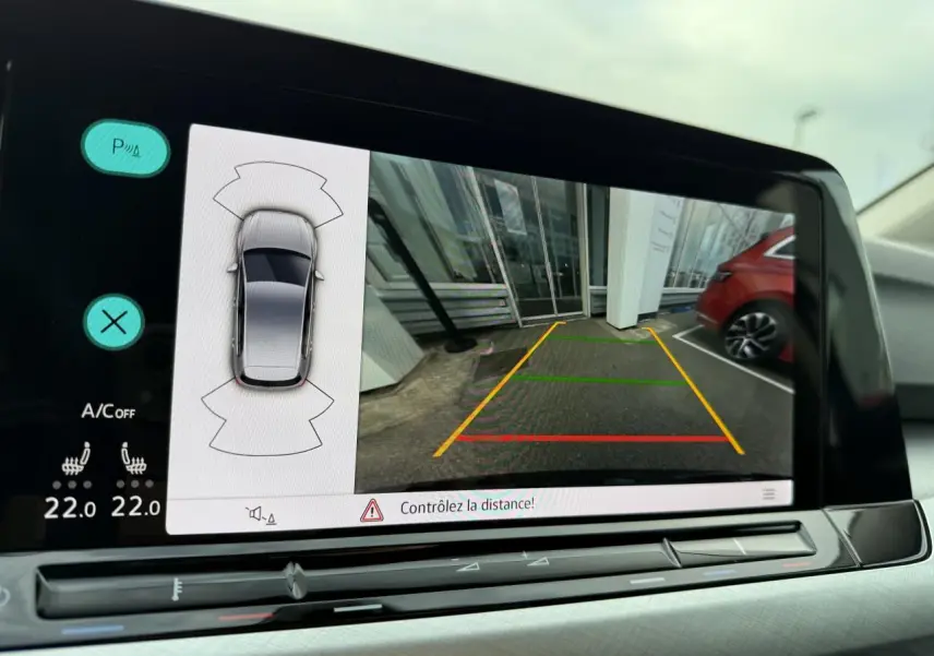 Écran de caméra de recul affichant l’aide au stationnement du Volkswagen Golf bleu Atlantique métallisé, vue intérieure.