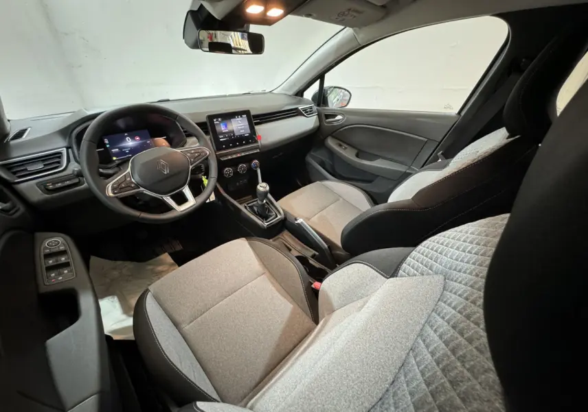 Intérieur de la Renault Clio 2025, vue côté conducteur, sièges gris clair et tableau de bord avec écran tactile central.