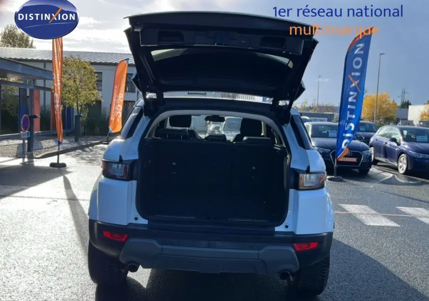 Vue arrière d'un Range Rover Evoque blanc 2017 avec coffre ouvert sur un parking ensoleillé.