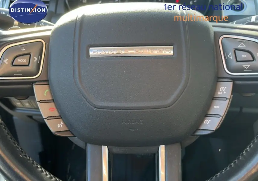 Gros plan sur le volant noir du Range Rover Evoque blanc, mettant en valeur les commandes intégrées et le logo central.