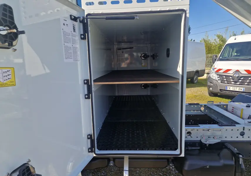 Vue de face du coffre blanc ouvert du châssis cabine Iveco Daily 35C16 avec benne acier et étagère intérieure visible.