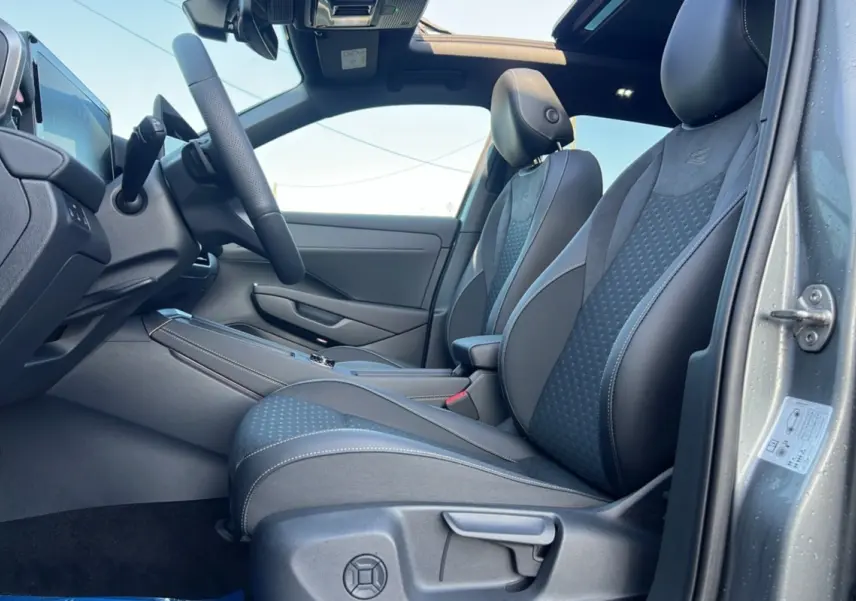 Vue intérieure côté conducteur du Volkswagen T-Roc gris loup 2026, sièges tissu R-Line avec surpiqûres blanches et toit ouvrant panoramique.