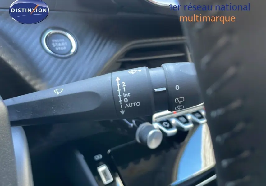 Gros plan sur la commande d’essuie-glace à gauche du volant d’une Peugeot 208 noire, avec bouton start en arrière-plan.