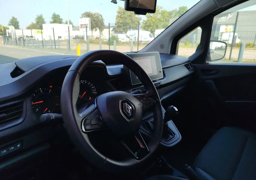 Vue intérieure côté conducteur du Renault Kangoo 2023, volant multifonction et écran tactile central visibles.