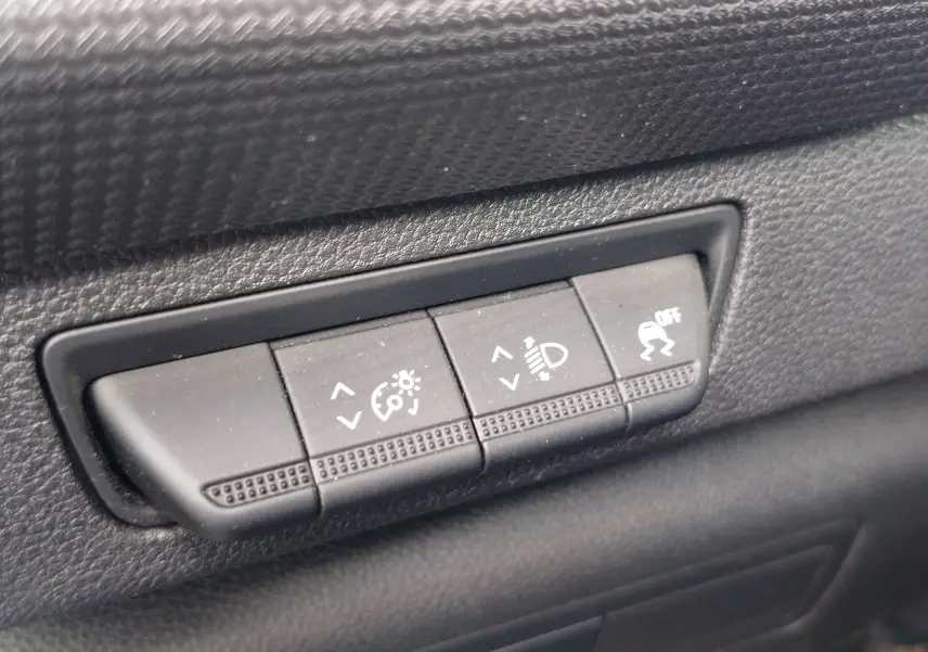 Gros plan sur les boutons de réglage d'éclairage et de contrôle de stabilité dans l'habitacle noir du Renault Kangoo blanc.