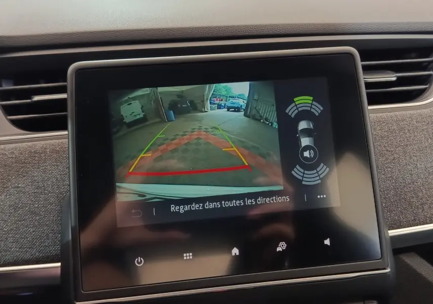 Écran tactile central montrant la caméra de recul et l’aide au stationnement arrière d’une Renault ZOE blanche.