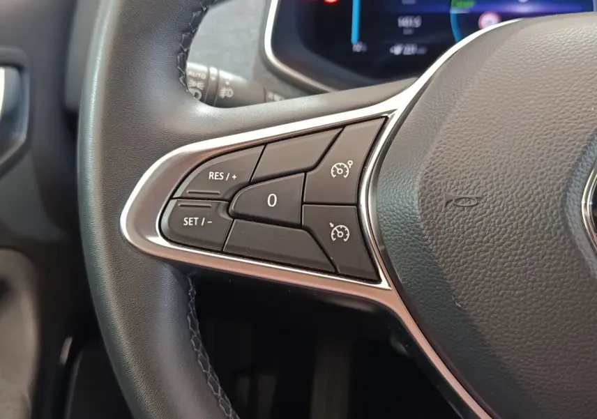 Gros plan sur les commandes de régulateur de vitesse au volant cuir noir d’une Renault ZOE Intens blanc.