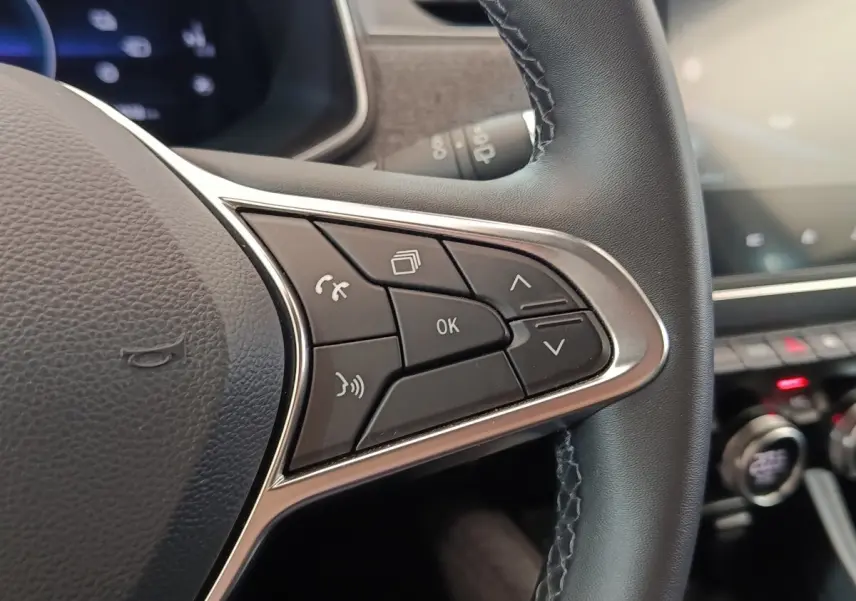 Gros plan sur les commandes multifonctions à droite du volant cuir noir de la Renault ZOE Intens blanc, tableau de bord en arrière-plan flou.