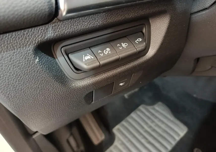 Gros plan sur les commandes d'assistance à la conduite à gauche du volant dans l'habitacle noir de la Renault ZOE blanche.