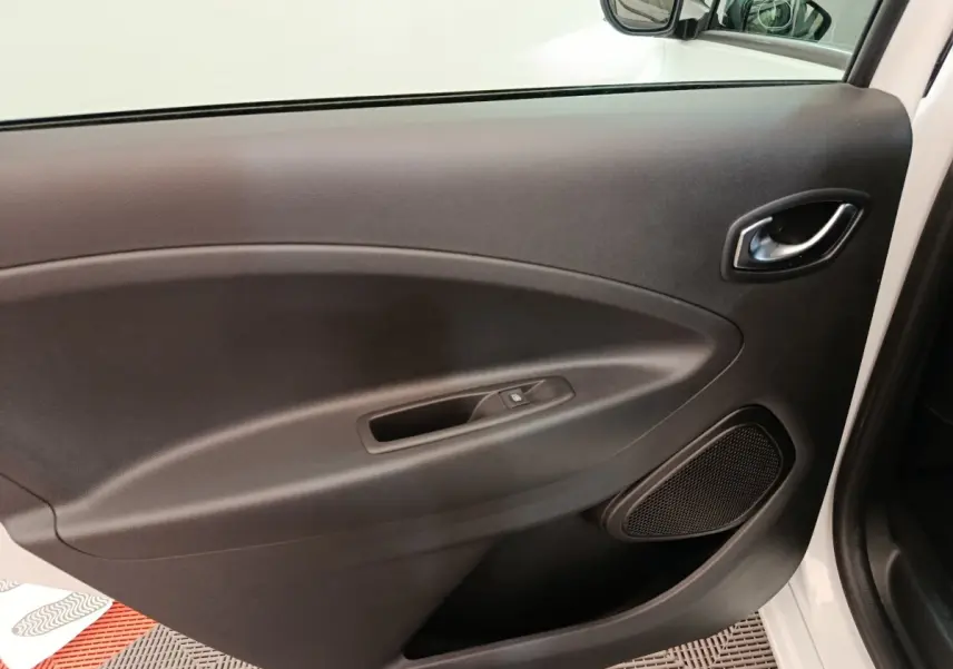 Vue intérieure de la porte avant droite noire de la Renault ZOE Intens R110 blanche, avec poignée et haut-parleur intégré.