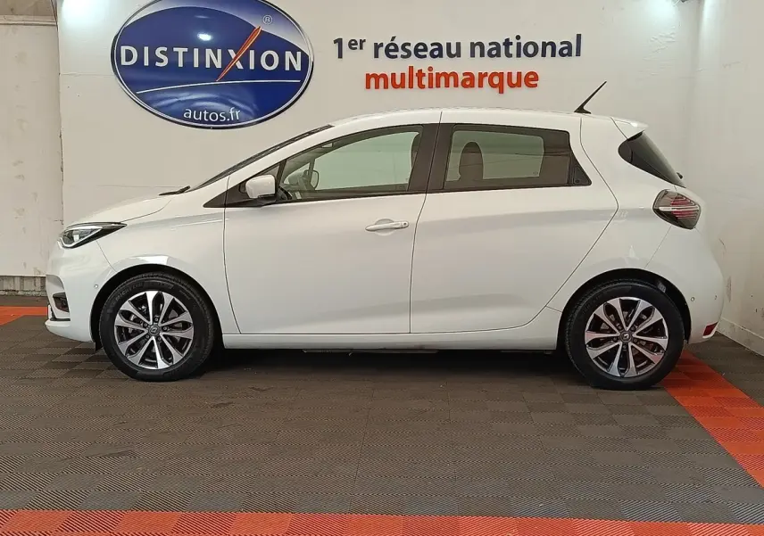 Profil droit d'une Renault ZOE Intens R110 blanche, avec jantes alliage et antenne de toit visible, en intérieur showroom.