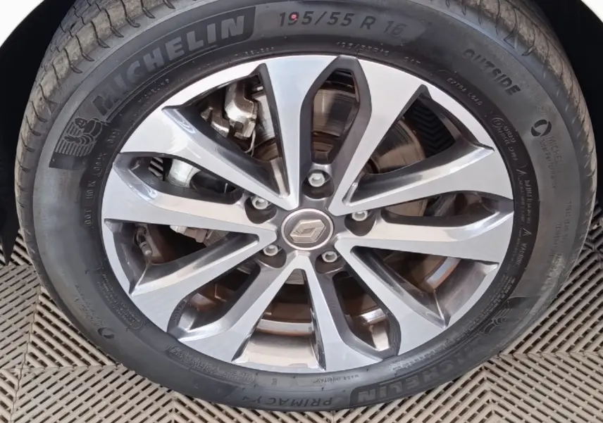 Gros plan sur la jante alliage gris et noir avec logo Renault au centre, montée sur pneu Michelin d’une Renault ZOE blanche.