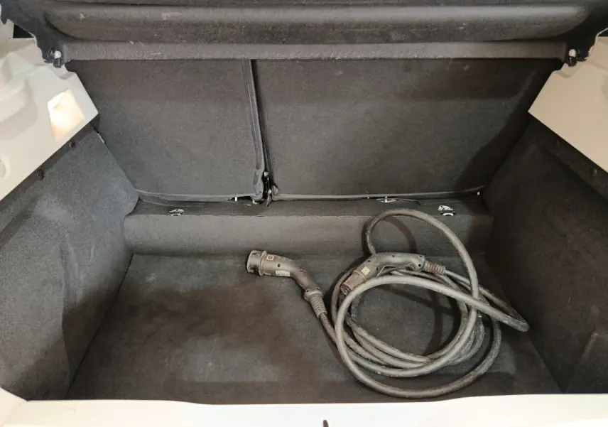 Coffre ouvert d'une Renault ZOE blanche avec câble de recharge électrique enroulé à l'intérieur.