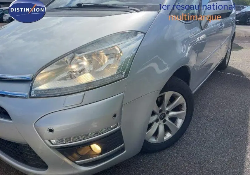Vue 3/4 avant droit d'une Citroën C4 Picasso gris alu métal avec feux allumés et jantes alliage visibles.