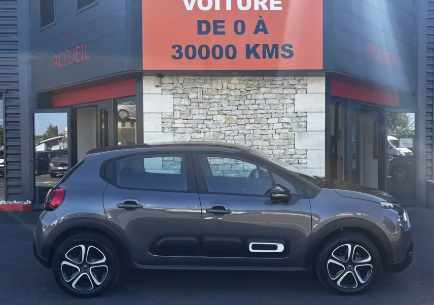 Vue profil côté gauche d'une Citroën C3 gris foncé 2024 avec protections latérales noires et jantes stylisées.