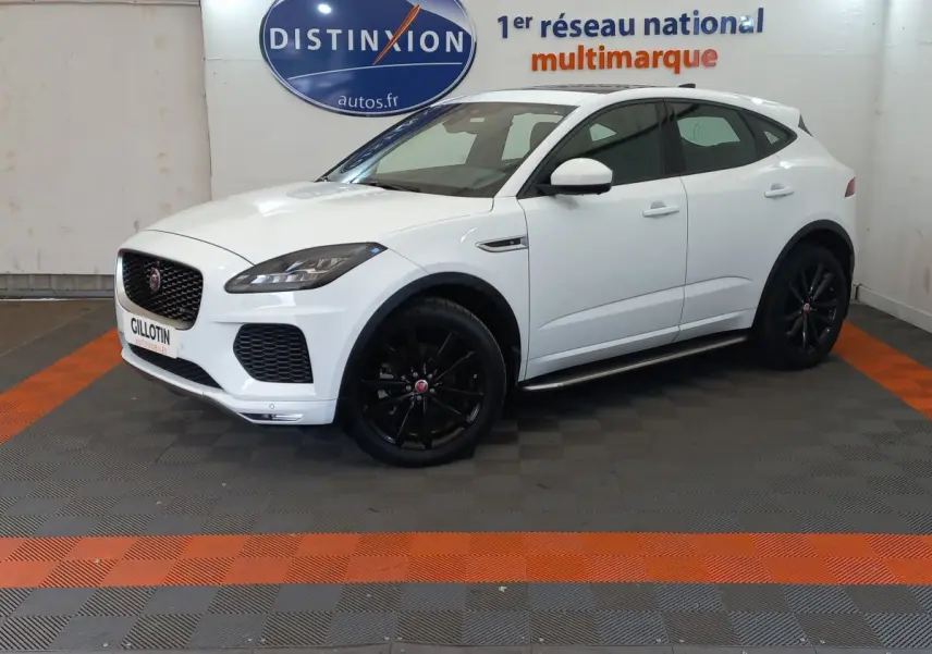 Jaguar E-PACE blanc vue 3/4 avant droit, roues noires, dans un showroom avec sol gris et bandes orange.