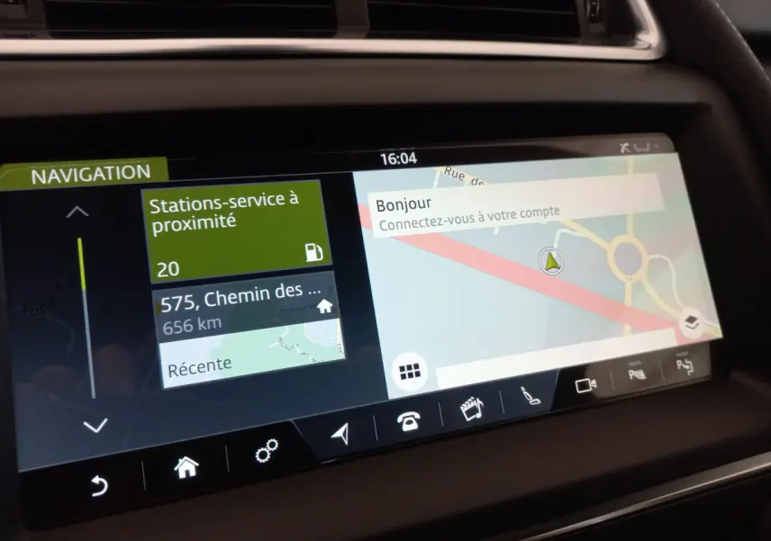Écran tactile de navigation du tableau de bord du Jaguar E-PACE blanc, affichant carte et stations-service à proximité.