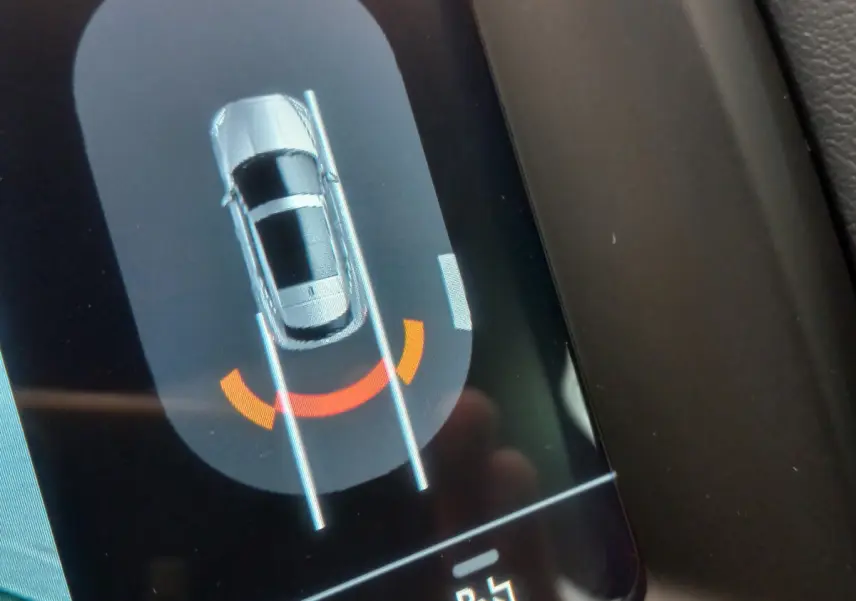 Affichage tactile montrant le Jaguar E-PACE blanc en vue aérienne avec assistance au stationnement arrière active.