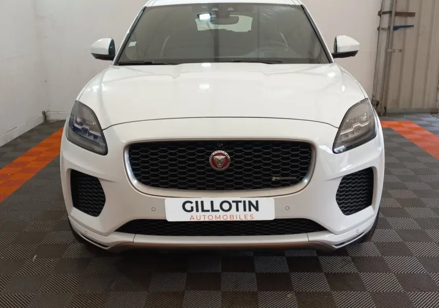 Vue frontale d'un Jaguar E-PACE blanc avec calandre noire et logo Jaguar bien visible, stationné en intérieur.