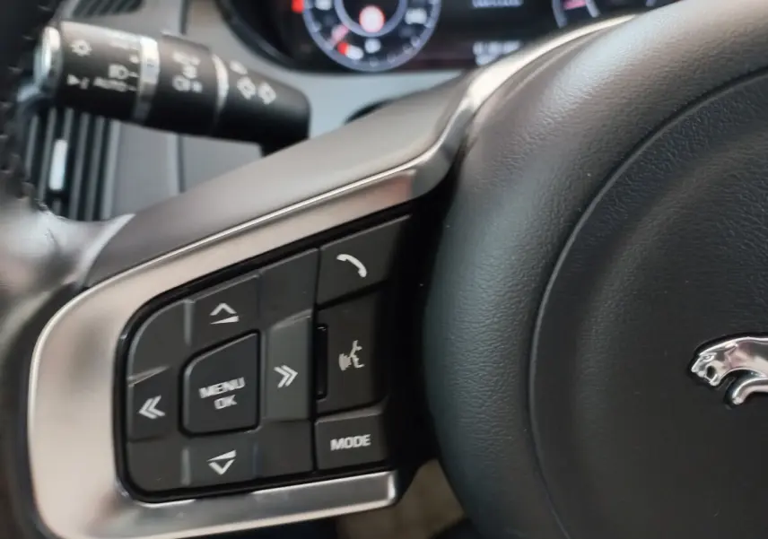 Gros plan sur les commandes gauche du volant cuir noir du Jaguar E-PACE blanc, avec logo jaguar visible.