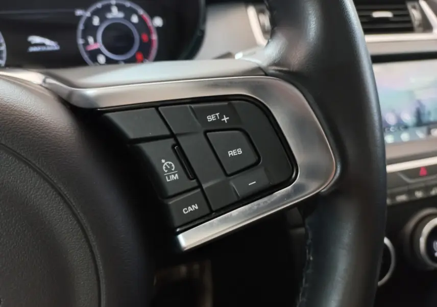 Gros plan sur les commandes de régulateur de vitesse au volant cuir noir d'une Jaguar E-PACE blanc 2019.