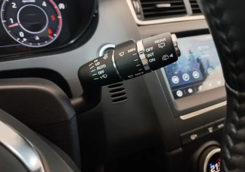 Gros plan sur la commande d’essuie-glace à gauche du volant dans l’habitacle sombre d’une Jaguar E-PACE blanc.