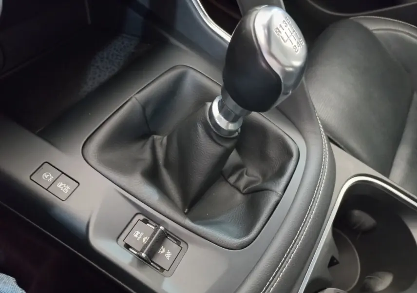 Gros plan sur levier de vitesse manuel noir et console centrale grise dans l'habitacle du Jaguar E-PACE blanc.