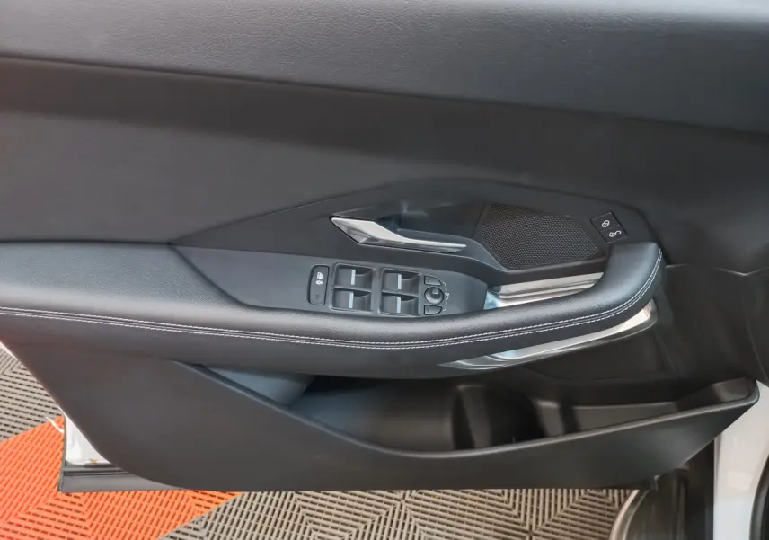 Gros plan sur la porte côté gauche de la Jaguar E-PACE blanche, avec commandes des vitres et poignée argentée.