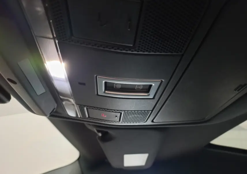 Vue en contre-plongée du panneau de commande de toit noir du Jaguar E-PACE blanc, avec éclairage intérieur allumé.