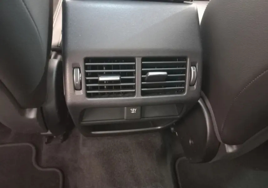 Vue rapprochée des aérateurs arrière noirs et prise 12V entre les sièges avant d'une Jaguar E-PACE blanche.