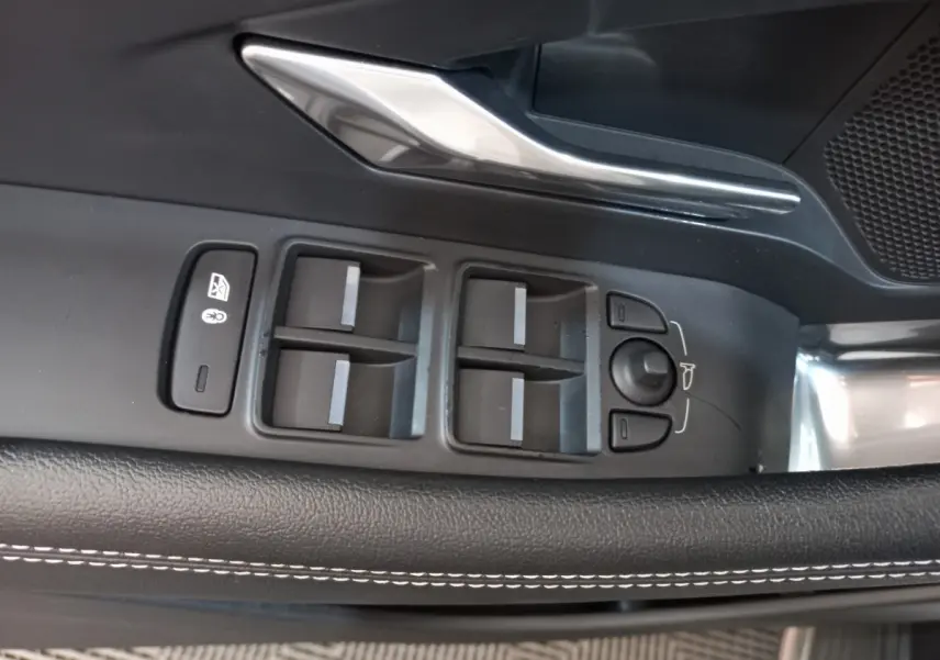 Gros plan sur les commandes de lève-vitres et rétroviseurs côté conducteur du Jaguar E-PACE blanc, avec surpiqûres blanches.