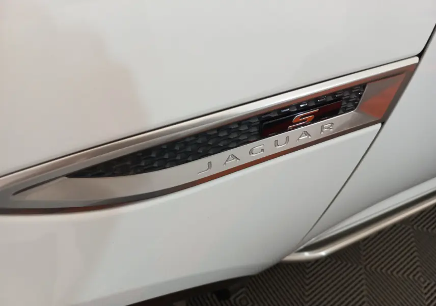 Gros plan sur l'emblème latéral "S" noir et orange du côté droit d'une Jaguar E-PACE blanche.