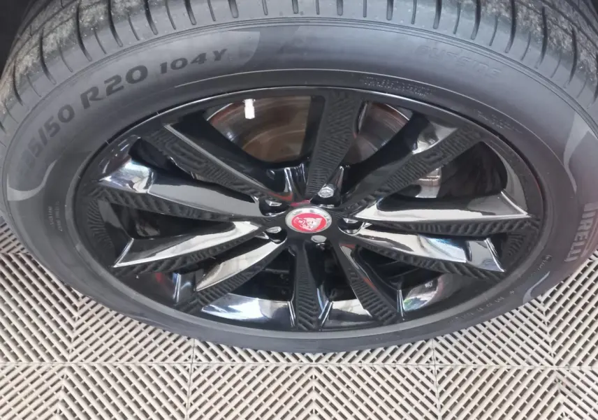 Gros plan sur la jante noire brillante avec logo Jaguar rouge d'un Jaguar E-PACE blanc, pneu Pirelli visible.