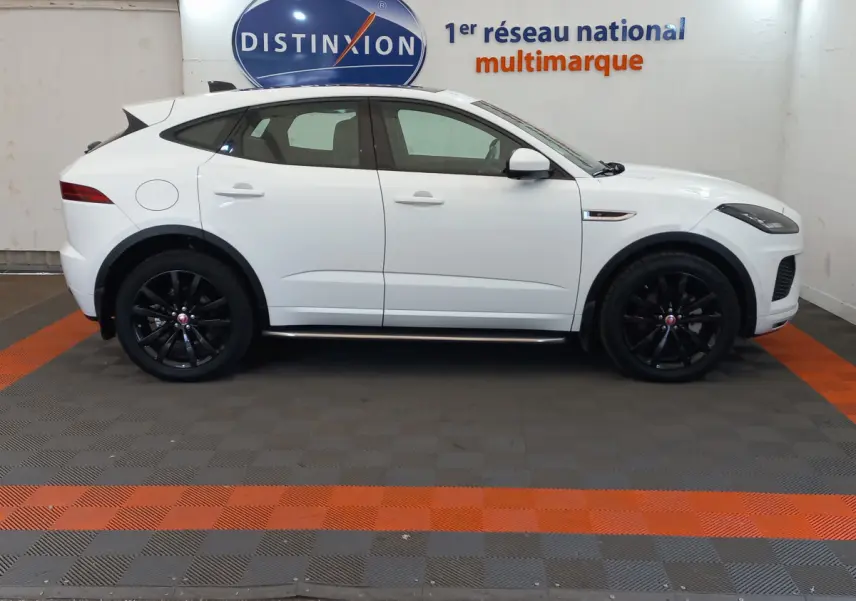 Jaguar E-PACE blanc vue de profil côté gauche avec jantes noires dans un showroom multimarque.