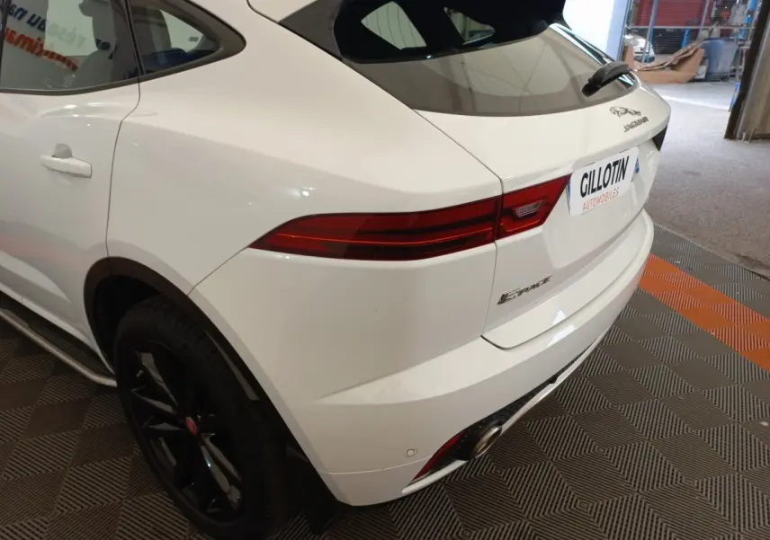 Vue 3/4 arrière droite d'un Jaguar E-PACE blanc avec feux arrière allongés et jantes noires brillantes.