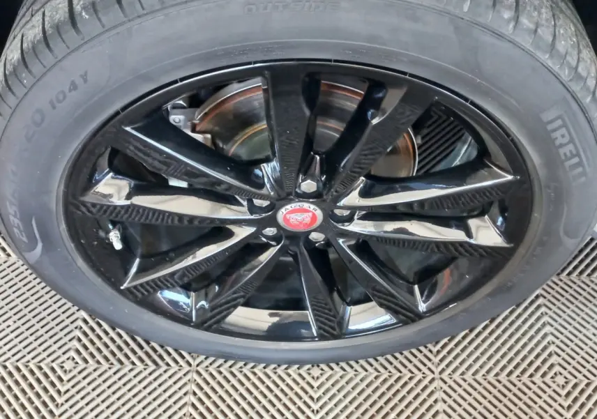 Gros plan sur la jante noire brillante d'une Jaguar E-PACE blanche, mettant en valeur le logo central rouge.