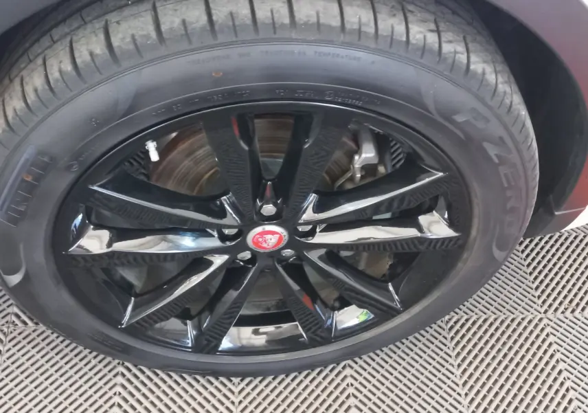Gros plan sur la roue avant droite du Jaguar E-PACE blanc, jante noire brillante avec logo Jaguar rouge au centre.