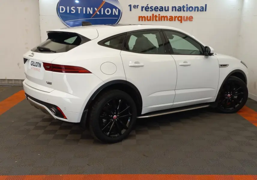 Vue de profil côté gauche d'un Jaguar E-PACE blanc avec jantes noires dans un showroom multimarque.