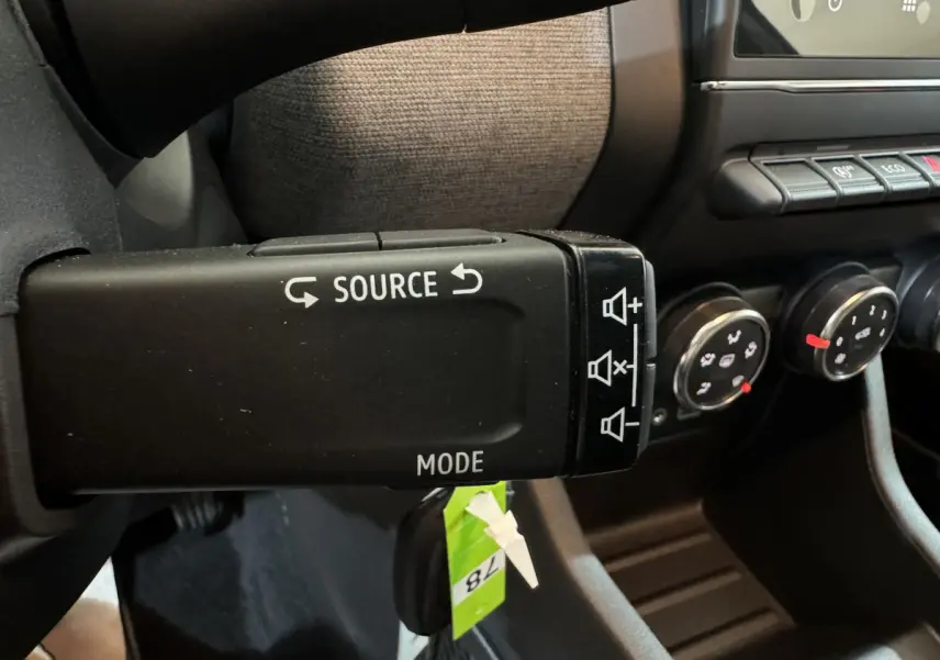 Gros plan sur la commande multimédia au volant d'une Renault Clio gris clair, avec boutons source et mode visibles.