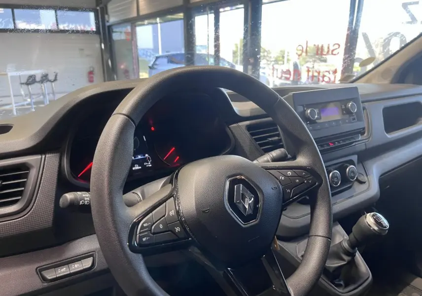 Vue intérieure centrée sur le volant et tableau de bord du Renault Trafic Fourgon gris foncé, avec levier de vitesse manuel.
