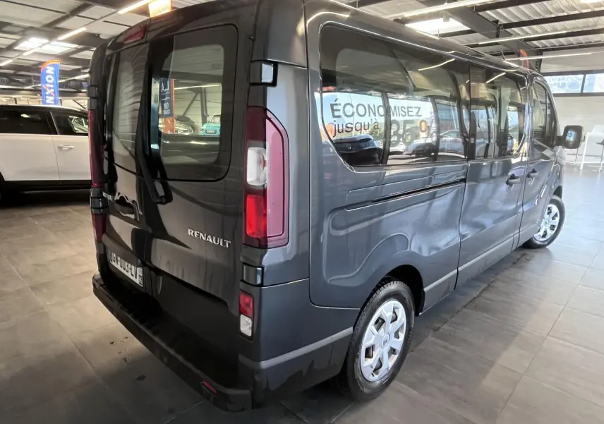 Vue 3/4 arrière droite d’un Renault Trafic Fourgon gris foncé avec vitres latérales teintées en showroom.