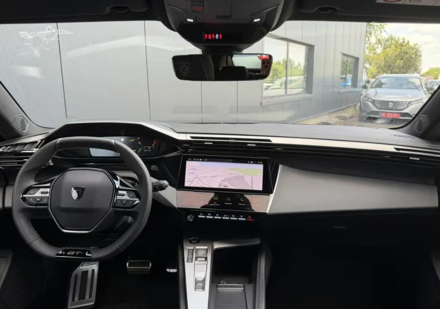 Vue intérieure avant de la Peugeot 308 GT Hybrid 2026 gris Selenium, volant compact GT et écran tactile central.