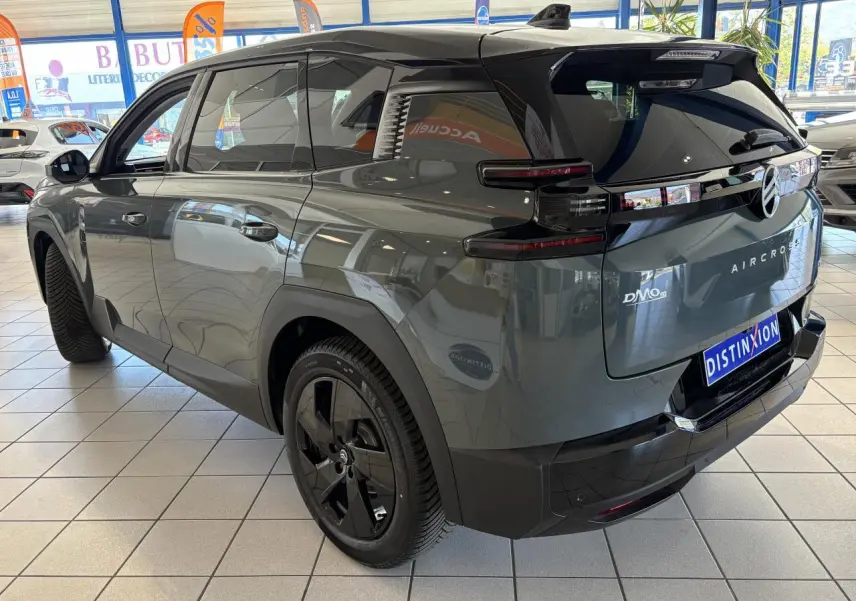 Vue 3/4 arrière droite du Citroën C5 Aircross vert métallisé avec jantes noires et feux arrière LED 3D en intérieur showroom.